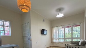 Una habitación amplia con suelo de baldosas, una mesa de comedor con sillas, un sofá, un televisor y una lámpara colgante.