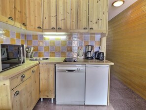 Una cocina compacta con armarios de madera, lavavajillas, microondas y cafetera.