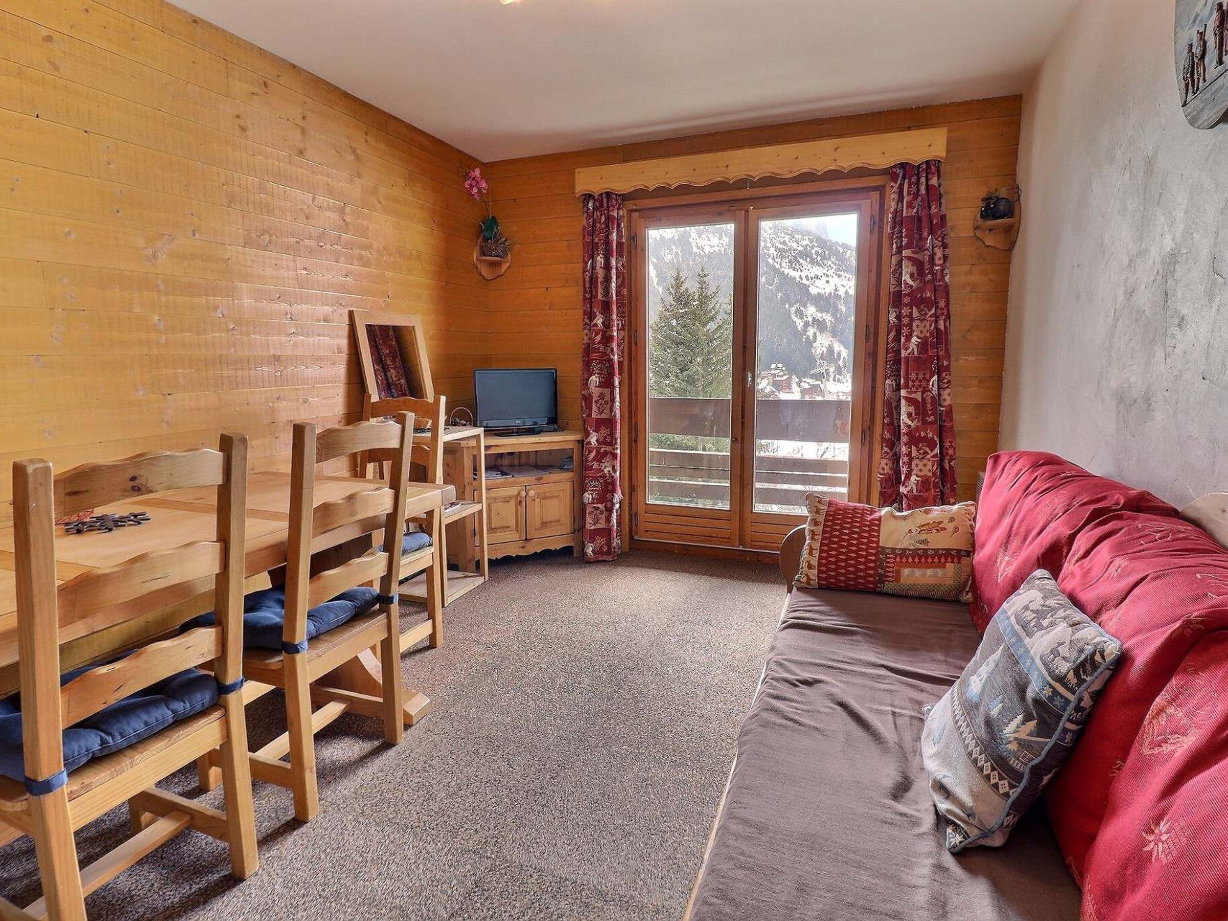 Una habitación acogedora con una mesa de madera, sillas, un sofá y un televisor.