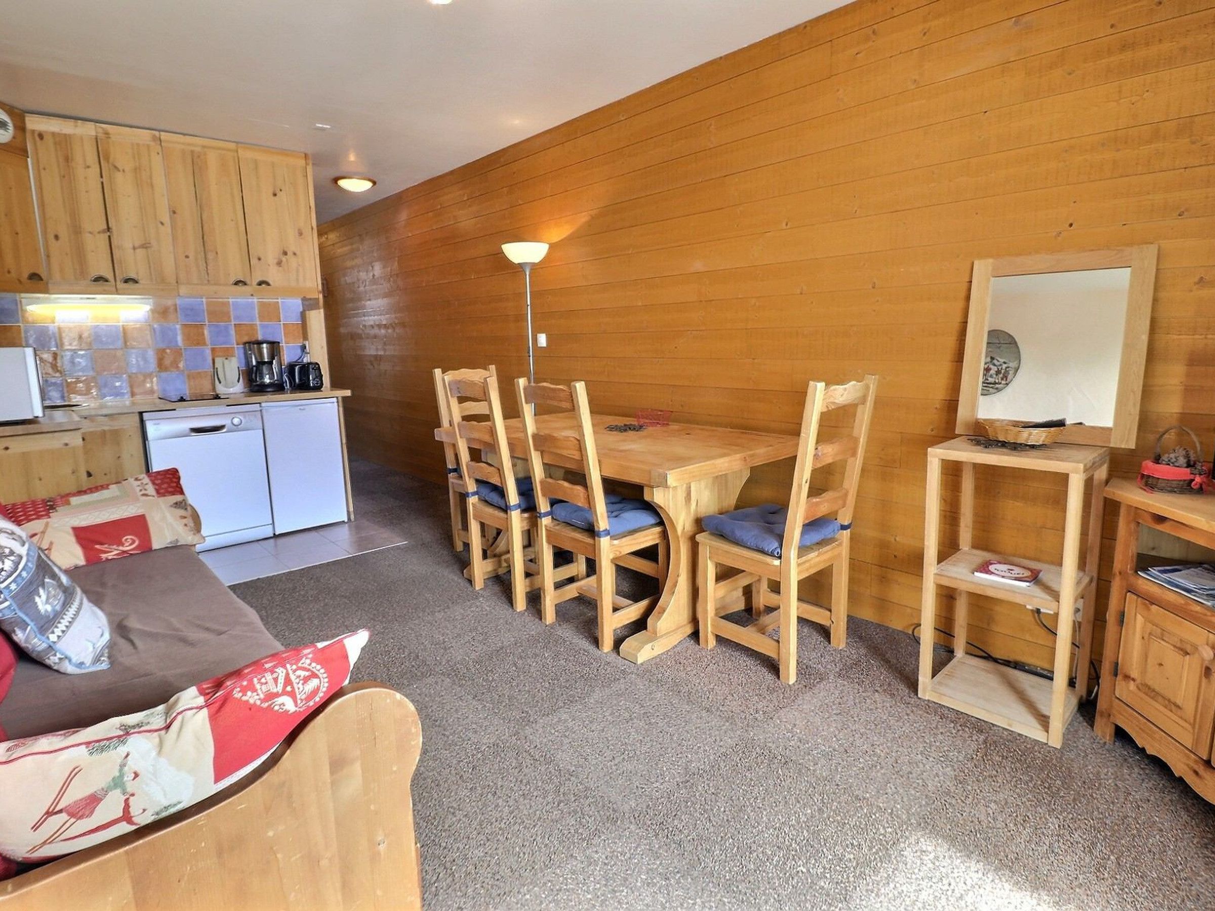 Eine gemütliche Küche mit Holzausbau, einem Esstisch mit Stühlen, einem kleinen Kühlschrank und einer Lampe.