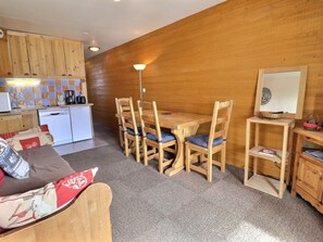 A cozy kitchen with wooden cabinets, a dining table with chairs, a small refrigerator, and a lamp.