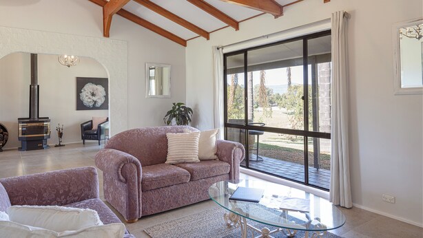 A living room with a sofa, a glass coffee table, a fireplace, and a large window with curtains. - The Homestead @ Hunter Gleann- Relax and Unwined In Rustic Luxury. (Pokolbin)