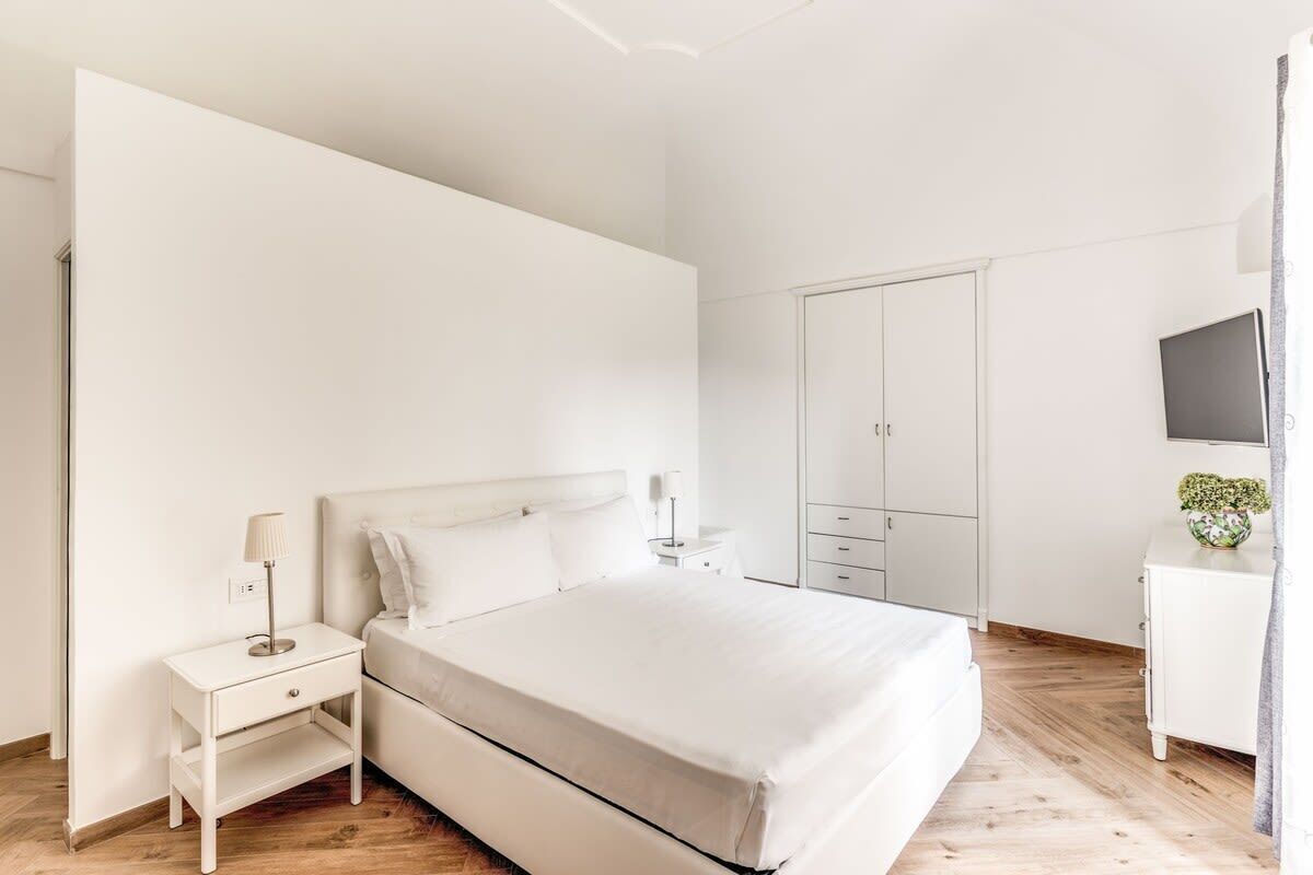 Une chambre à coucher minimaliste comprenant un lit, une table de chevet, une lampe, une armoire et un téléviseur posé sur un meuble.