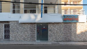 Un immeuble à la façade en pierre, avec une entrée dotée d’une porte en verre et une enseigne publicitaire indiquant : « Tropical is Aparthos ».