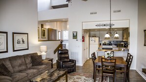 A spacious living room with a brown leather sofa, a wooden coffee table, and a dining area with a wooden table and chairs.
