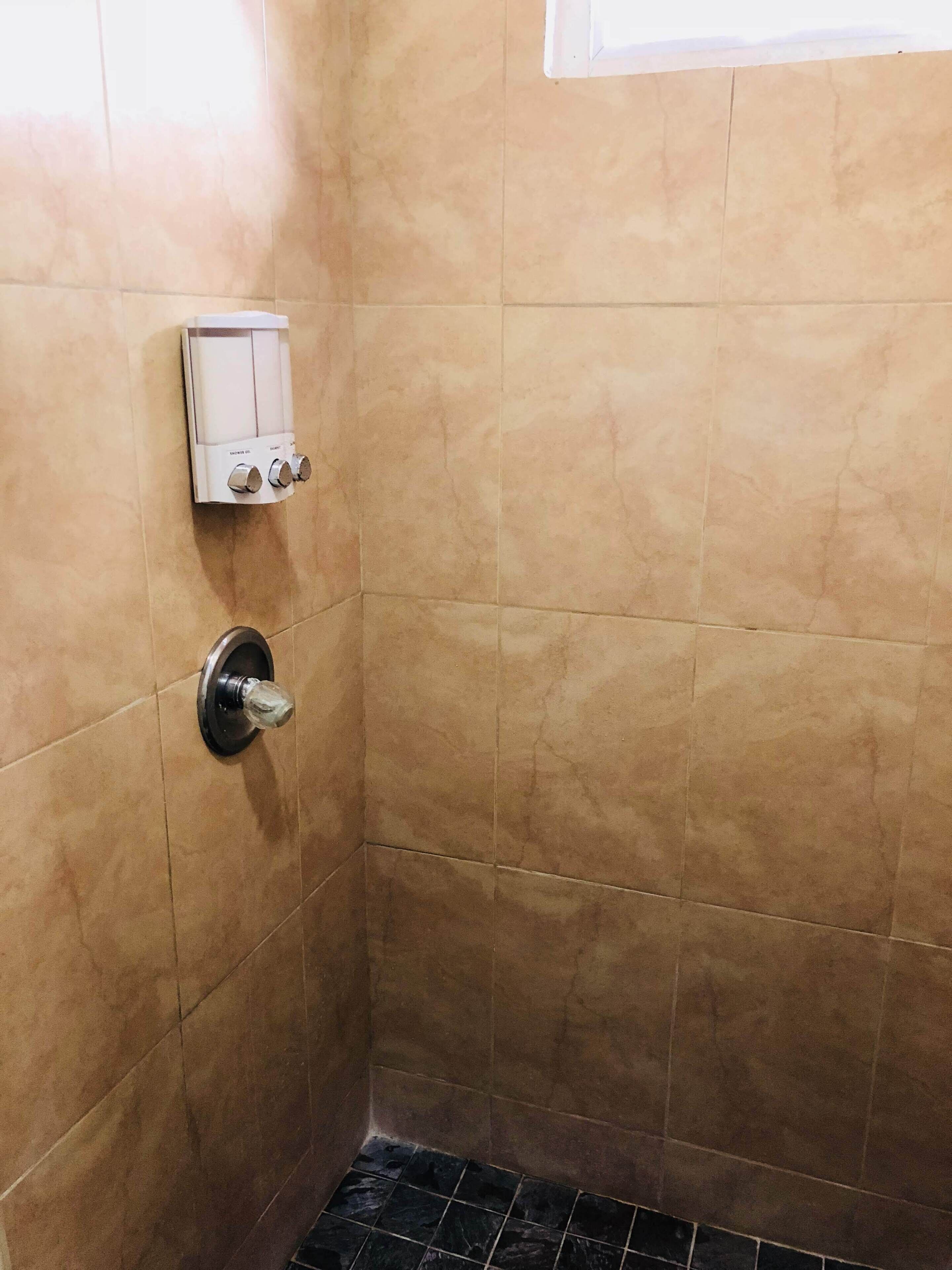 A corner of a bathroom with beige tiles, a wall-mounted faucet, and a control panel.