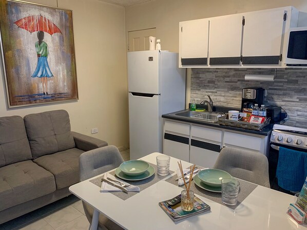 A modern kitchen with white cabinets, a white refrigerator, a stove, and a sink. There is a dining table with green plates and cutlery. - Homey Escape with Patio Access and FREE Laundry (Ponce)
