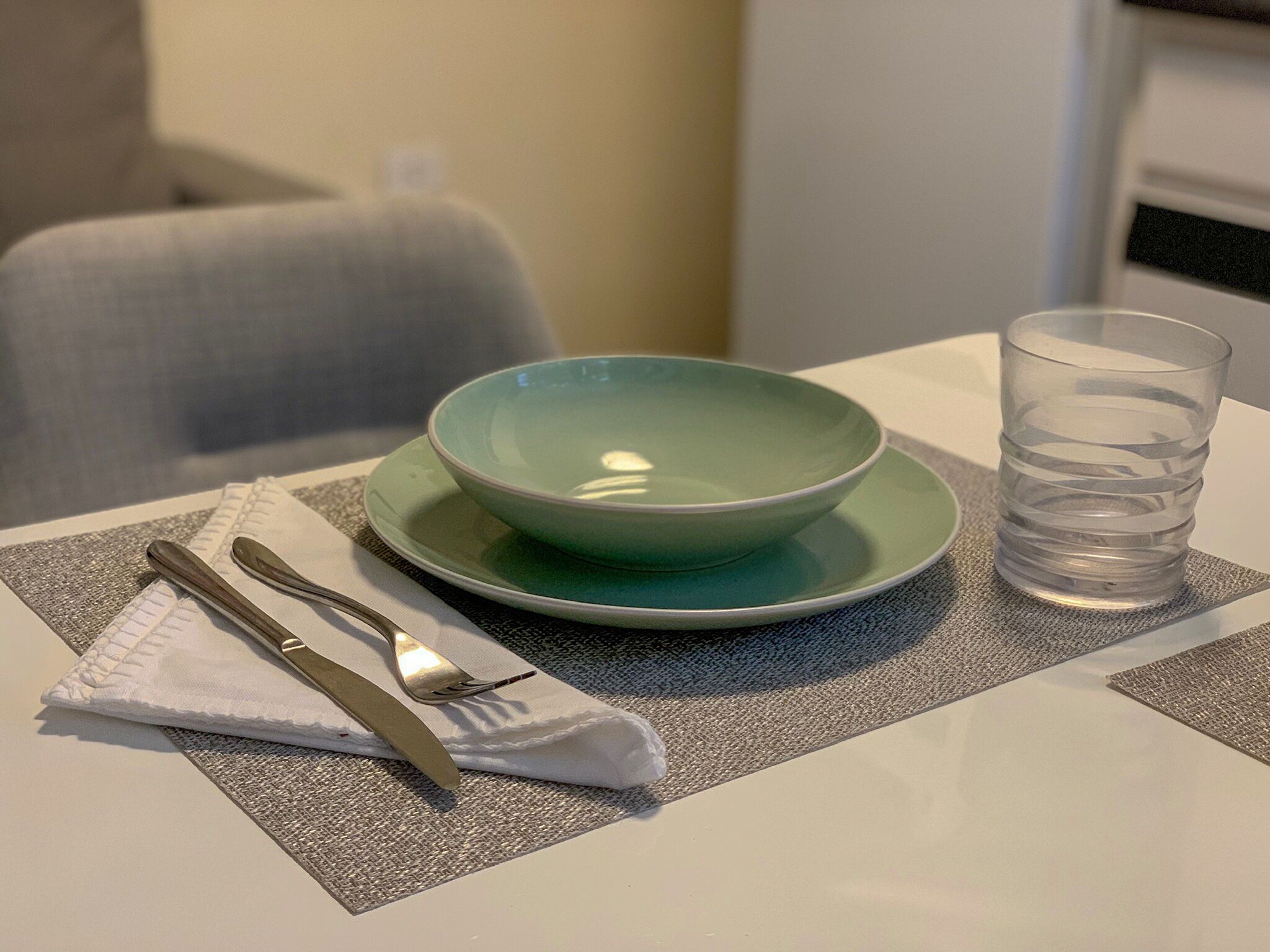 A table set with a green bowl, a glass of water, and cutlery on a placemat.