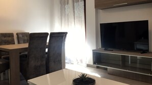 Una sala de estar moderna con comedor, un televisor de pantalla plana y una planta en la mesa de centro.