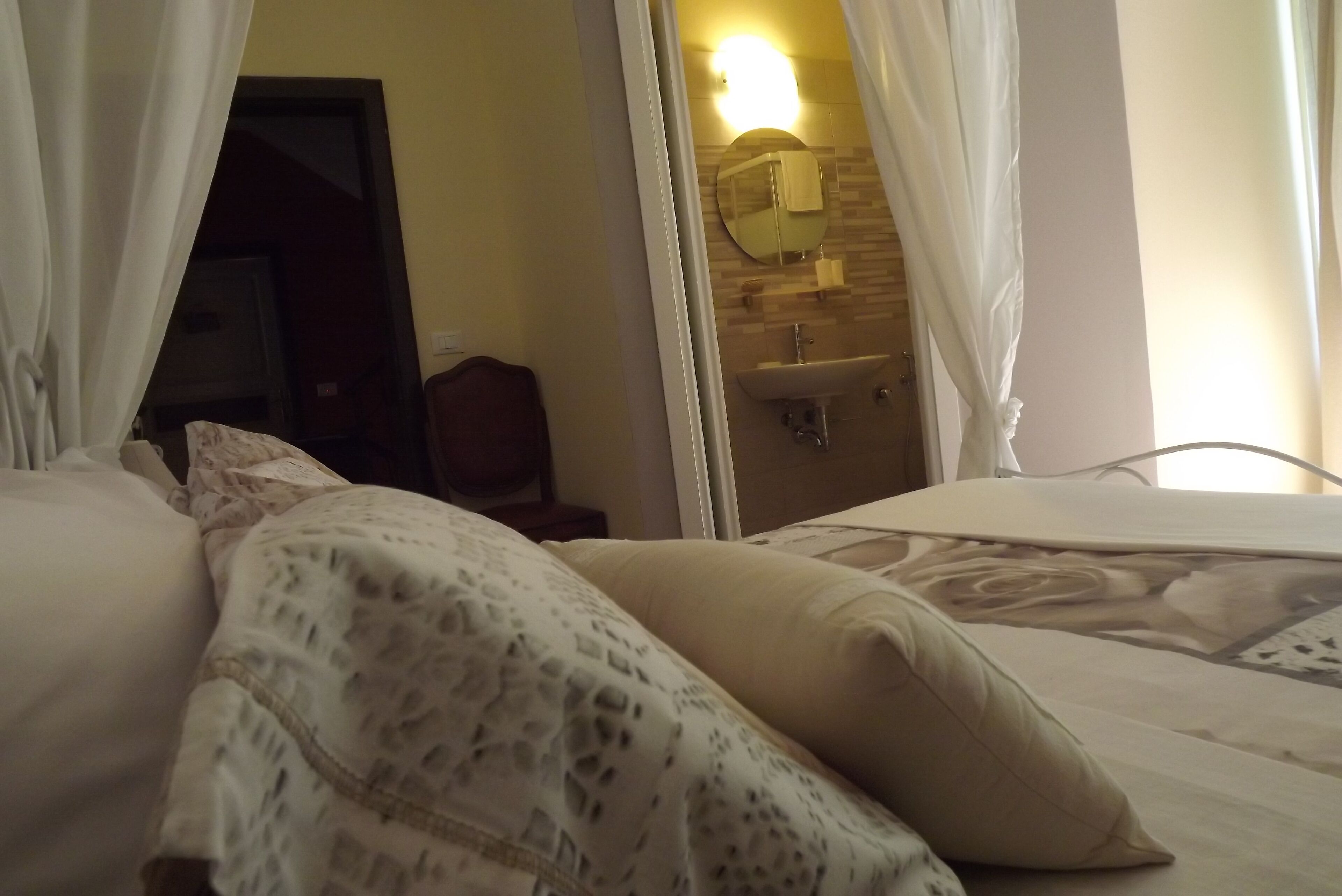 A hotel room with a bed, a bedside table, a mirror, and a bathroom visible through an open door.