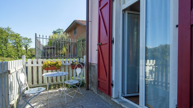 Eine Terrasse mit einem weißen Metalltisch und Stühlen, einer roten Tür und einem weißen Zierzaun.