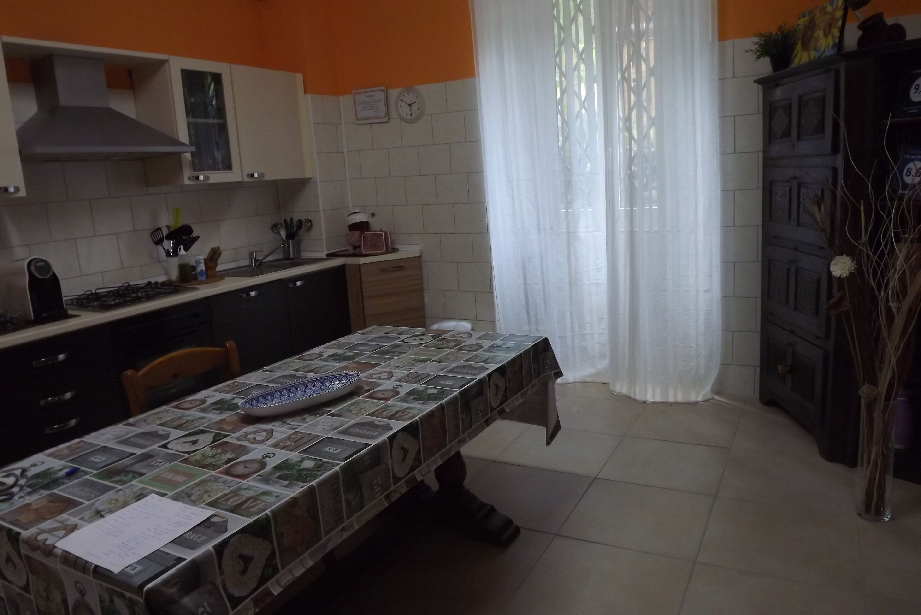 Une cuisine avec un mur recouvert de carreaux, une cuisinière et une table à manger recouverte d’une nappe à motifs.