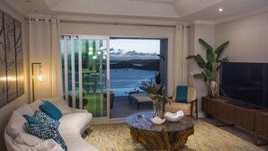 A modern living room with a sofa, a coffee table, a TV, and a large window offering a view of the sea. - Luxury villa with private pool, ocean views and private-access beach (St. George)