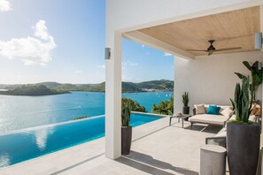 Une terrasse extérieure moderne, dotée d’une piscine donnant sur une magnifique baie, d’un ventilateur de plafond et de sièges confortables.