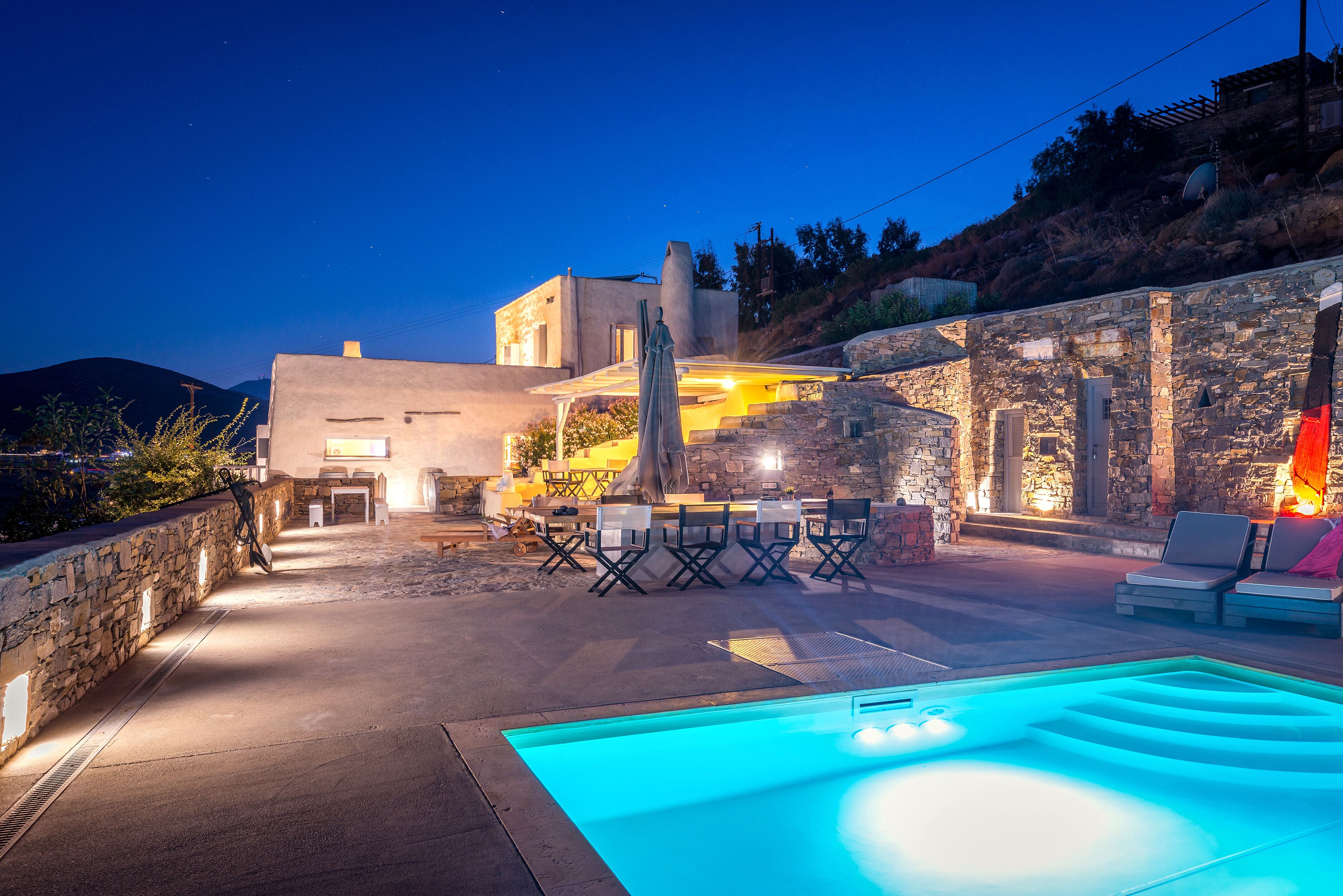 A pool area with a stone wall, outdoor seating, and a building in the background.