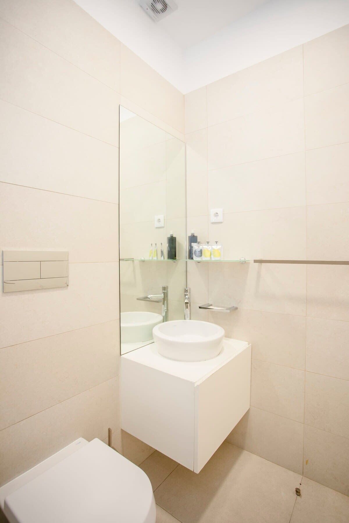 A modern bathroom with a large mirror, a white sink, and a toilet.