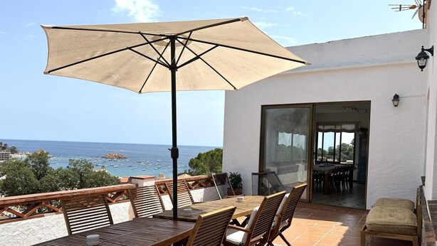 An outdoor patio with a table and chairs, a large umbrella, and a view of the sea. - BEAUTIFUL HOUSE SEA VIEWS (Tossa de Mar)