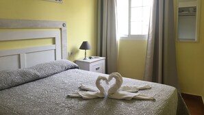 Ein Hotelzimmer mit Bett, Nachttisch, Lampe und einem Fenster mit Vorhängen.