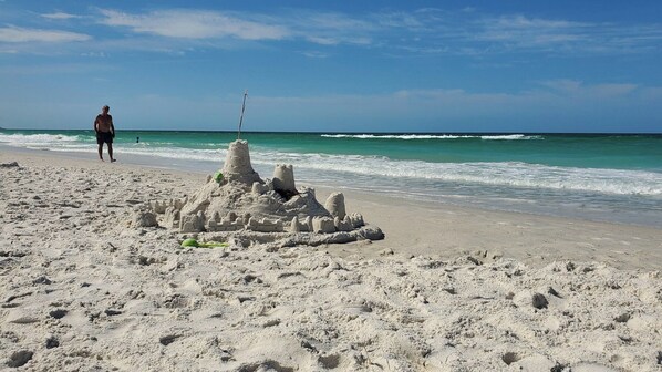 A sandy beach with a large sandcastle and a person standing in the background.