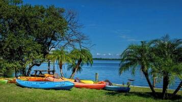 Un área con césped, varias kayaks alineados cerca del agua, rodeado de árboles.
