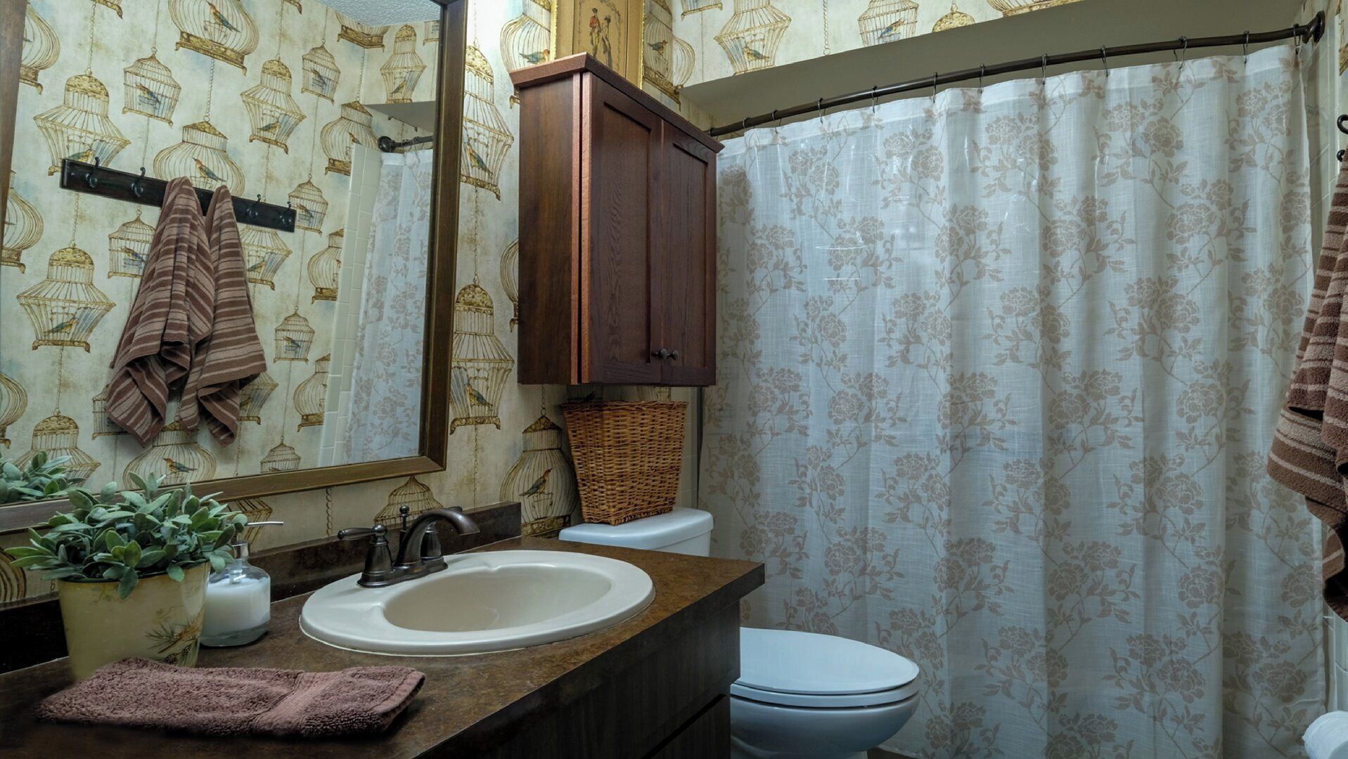 Un bagno con lavandino, specchio, mobiletto, water e tenda doccia.