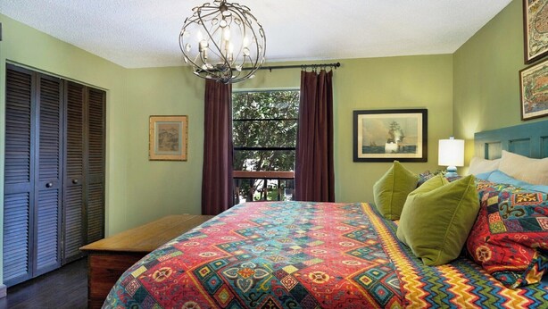 A bedroom with a large bed, a hanging light fixture, a window with curtains, and a door with louvered panels. - LAST MINUTE DEALS! FREE WIFI I  Banyan – Peaceful 1BR Getaway Near Beaches, Bays & Dining (Bradenton)
