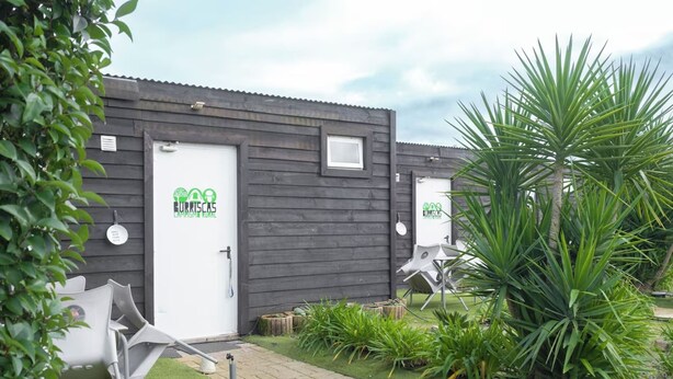 A building with two doors, each marked with a logo and the text "Burrasca Campsite". There are outdoor chairs and a tire on the ground. - Bungalow (Montemor-o-Novo)