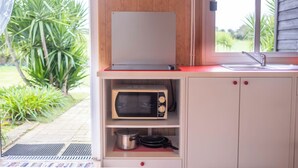 A compact kitchen with a microwave, a pot, and a pan on shelves. - Bungalow (Montemor-o-Novo)