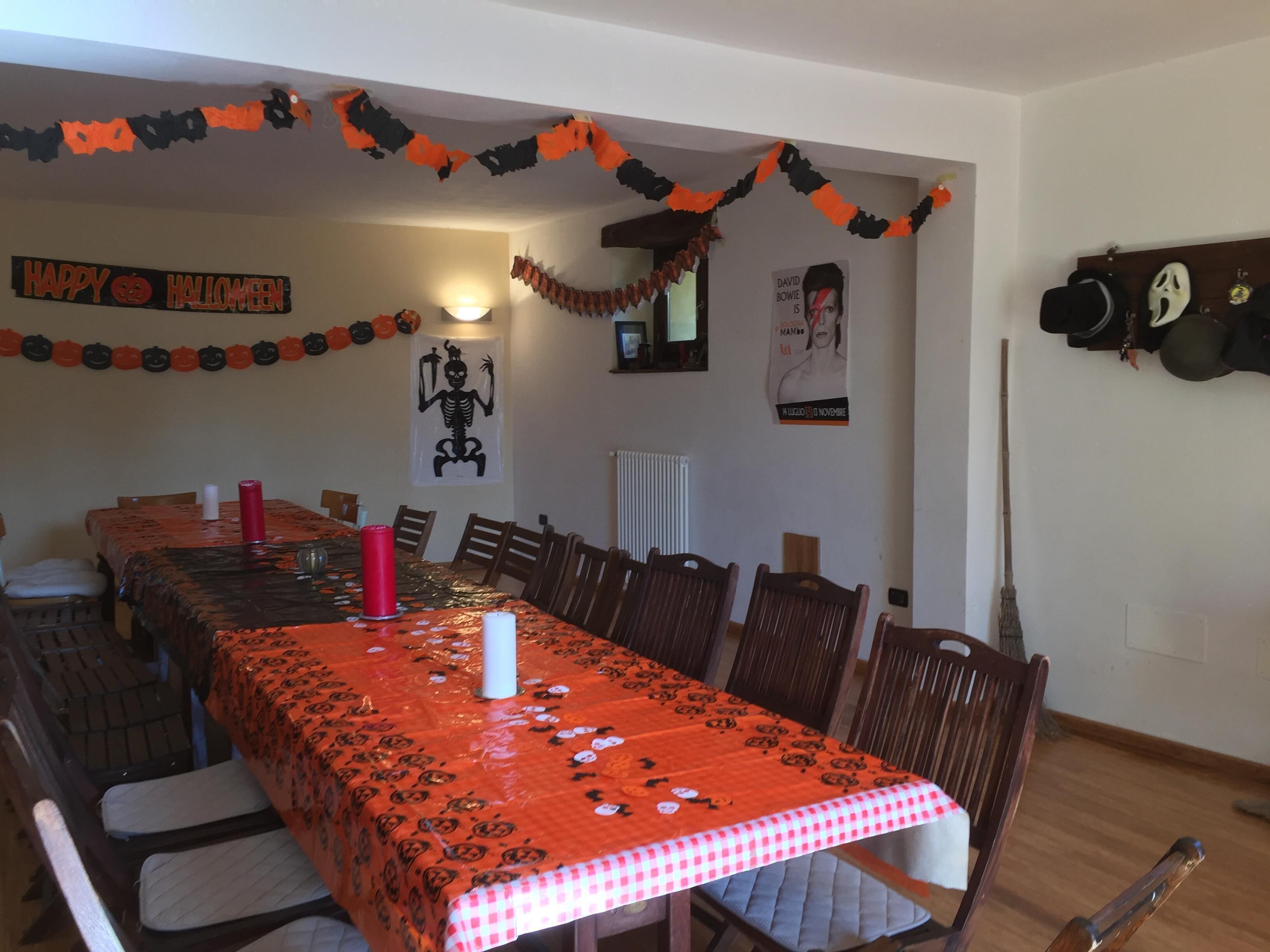 Un comedor con una mesa larga cubierta con un mantel de temática de Halloween, rodeada de sillas de madera.