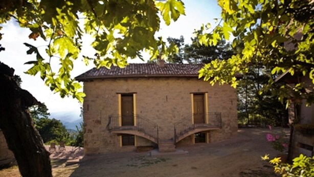 A stone building with a tiled roof, two doors, and a small staircase leading to a balcony.