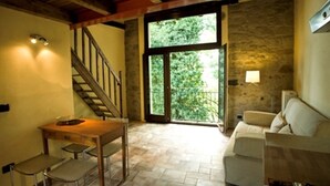 A room with a wooden staircase, a dining table with chairs, a sofa, and a large window with a view of greenery.