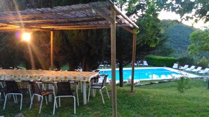 Un área de comedor al aire libre con una mesa, sillas, una pérgola y una piscina al fondo.
