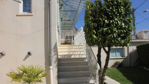 Una escalera con barandilla de metal que lleva a un balcón, rodeado de plantas en macetas y un cielo despejado.