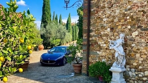 A stone building with a statue, a parked car, and potted plants. - Villa Carmignani, your home in Tuscany: exlusive use of villa, grounds and pool. (San Casciano in Val di Pesa)