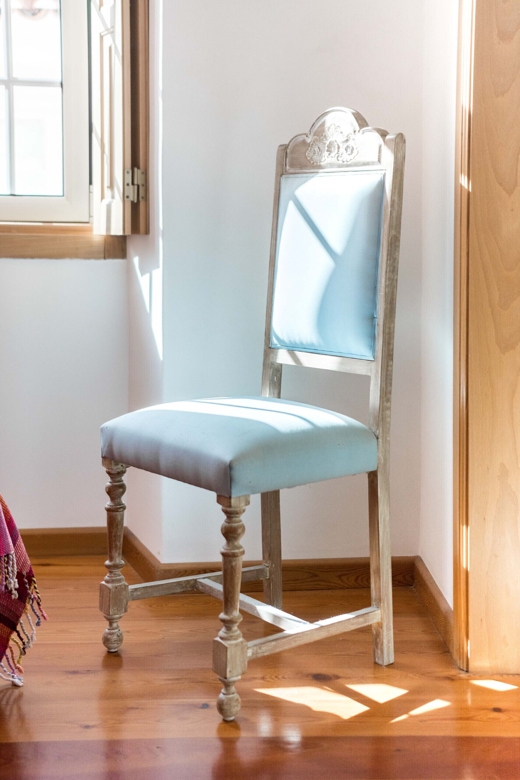Una silla de madera con un cojín azul claro en una habitación con piso de madera y un ventanal.