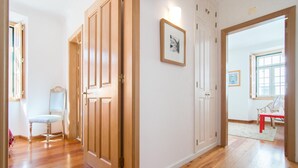 A hallway with wooden floors, a bench, and a door leading to another room. - Gomes Freire Terrace (Cascais)