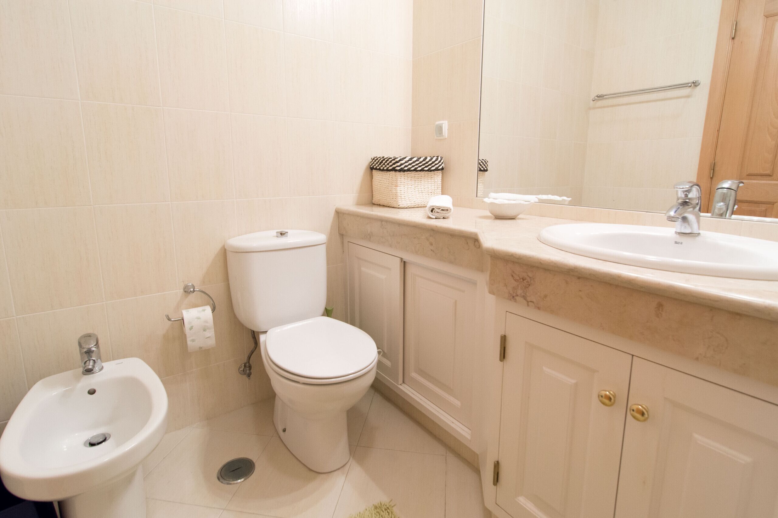 Un baño con bidé, inodoro, lavabo y espejo.