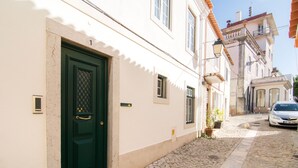 A narrow cobblestone street with a green door and a white building with a balcony. - Gomes Freire Terrace (Cascais)