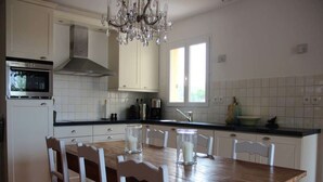 A kitchen with white cabinets, a wooden dining table, and chairs. - Villa du Moulin with private swimming pool (Saumane de Vaucluse)