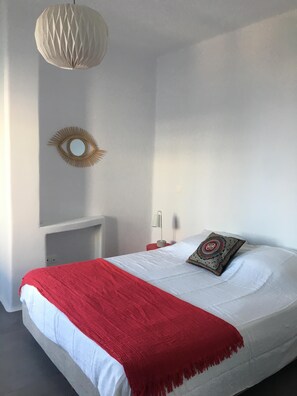 Un lit avec un couvre-lit rouge, un coussin décoratif, un miroir fixé au mur et un luminaire suspendu.