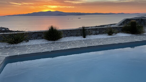 Una piscina con borde de piedra y vista al mar al atardecer.
