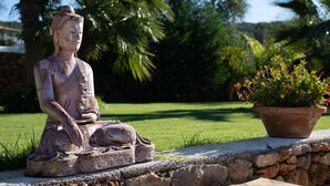 Une statue de Bouddha en pierre, placée dans un jardin, avec une plante en pot à proximité.