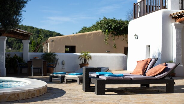 Un espace aménagé au bord de la piscine, avec des chaises longues, un jacuzzi et une vue sur un immeuble doté d’un balcon.