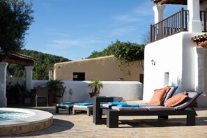 Un espace aménagé au bord de la piscine, avec des chaises longues, un jacuzzi et une vue sur un immeuble doté d’un balcon.