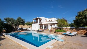 Une piscine avec des chaises longues, une terrasse en pierre et un bâtiment blanc doté d’un balcon.