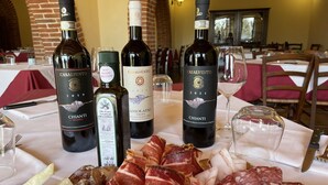 Et bord med tre flasker Casalvento vin, en flaske ekstra jomfru olivenolie og forskellige typer af lufttørret kød.