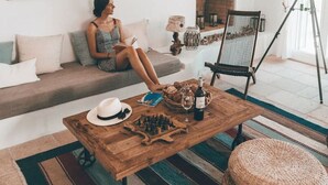 A cozy living room with a sofa, a wooden coffee table with chess pieces, a telescope, and framed artwork on the wall. - On The Rocks - The Two Rocks - Serviced Villa (Ios)