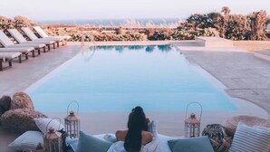 A poolside area with lounge chairs, a person relaxing, and a view of the ocean. - On The Rocks - The Two Rocks - Serviced Villa (Ios)