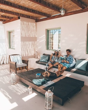 A room with a wooden ceiling, a sofa, a coffee table, and two people sitting on the sofa.
