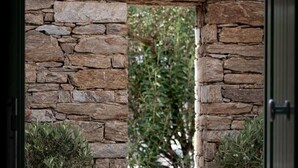 A stone wall with a small window, potted plants, and a door frame. - On The Rocks - The Two Rocks - Serviced Villa (Ios)